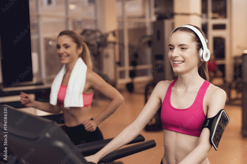 Woman and girl running on treadmill at the gym. They look happy, fashionable and fit.