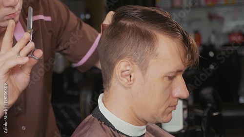 Close-up of barber cuts the hair by scissors at barbershop..