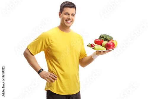 Young man holding a plate of vegetables and fruit