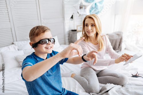 Virtual technology. Happy delighted nice boy smiling and looking at his hands while wearing digital virtual glasses