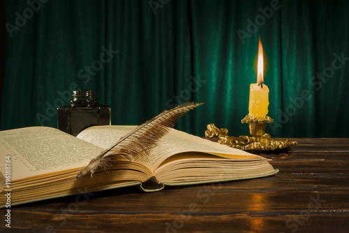 Education and writing concept, pen lying on the book, inkwell and candle