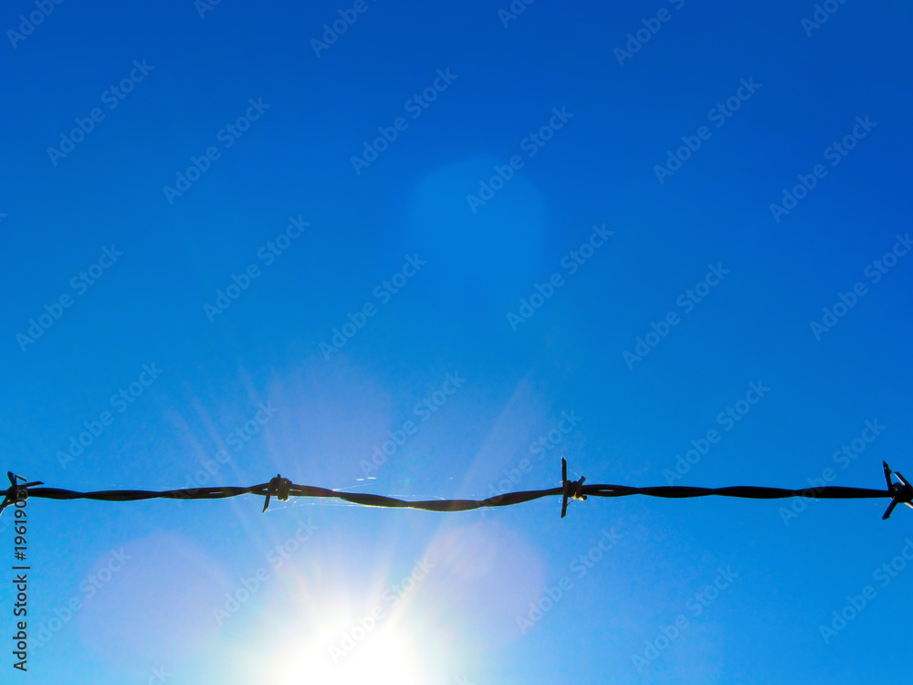 Wire fencing against a blue sky and sun.
Black horizontal line of sharp-cut silhouette and bright sunlight. Wire fencing against a blue sky and sun.
Black horizontal line of sharp-cut silhouette and bright sunlight.