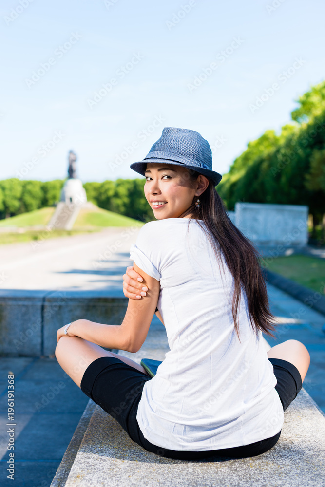 Fototapeta premium Young woman holding a blue hat above the head while sitting in the park in summer