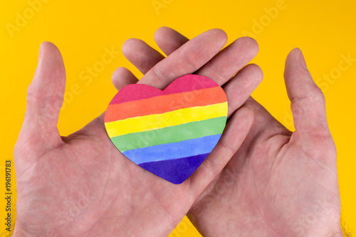 heart LGBT flag rainbow in the hands yellow background