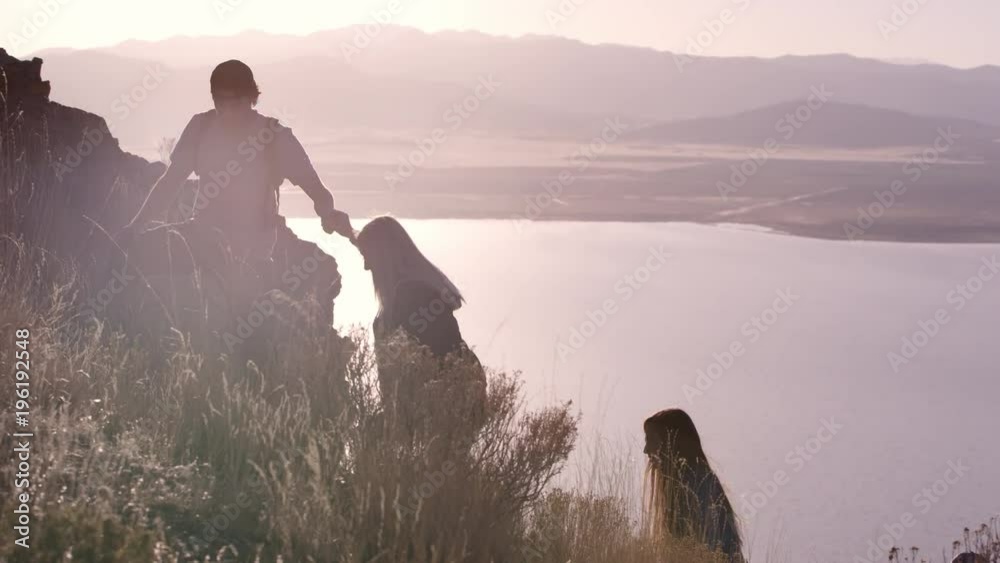 Slow motion of man helping people up the steep trail as women reach out for his hand and he pulls them up.