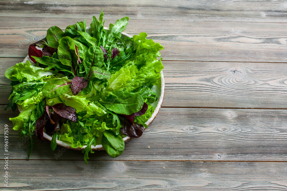 Leaves of fresh lettuce, arugula, spinach and beet sprouts in a plate on a wooden background. Leaves of fresh lettuce, arugula, spinach and beet sprouts in a plate on a wooden background.