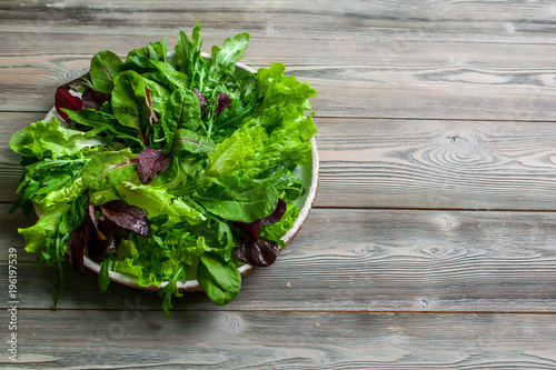 Leaves of fresh lettuce, arugula, spinach and beet sprouts in a plate on a wooden background.