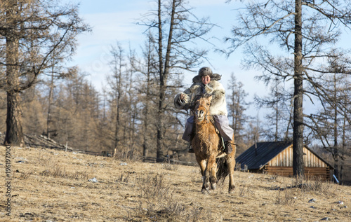 mongolian man dressed in wolfskin clothing riding a horse in a forest photo