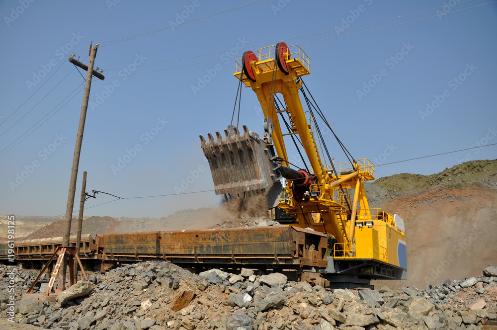 A large yellow excavator loads ore into a railway car A large yellow excavator loads ore into a railway car