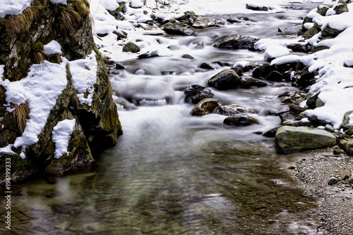 Winter landscape with snow covered valley and frozen river, with small waterfalls shot on long exposure