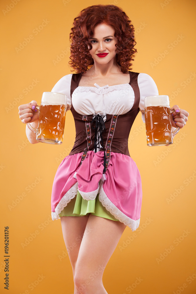 Young sexy Oktoberfest waitress, wearing a traditional Bavarian dress,  serving big beer mugs on yellow background. Stock Photo | Adobe Stock