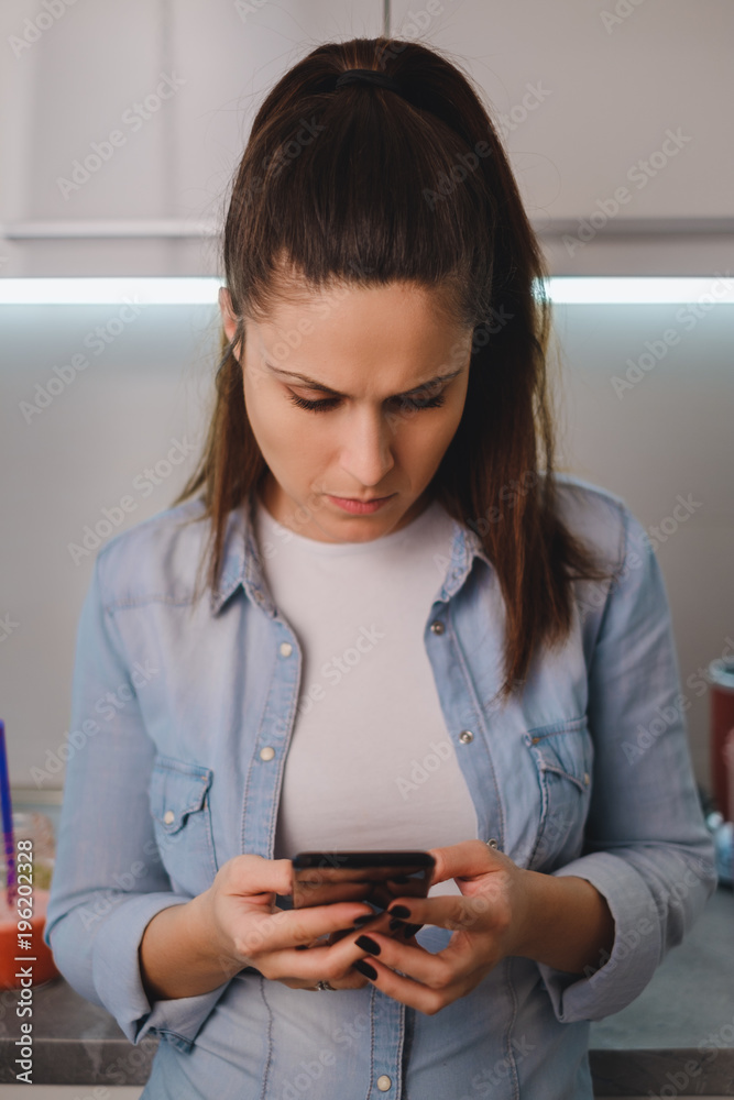 Angry girl looking at mobile phone in the kitchen Angry girl looking at mobile phone in the kitchen