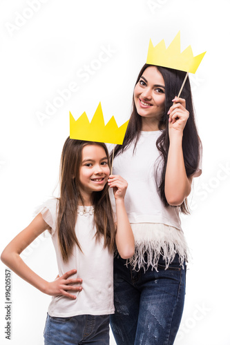 Smiling Mother and daughter posing with paper crowns on stick isolated on white background photo