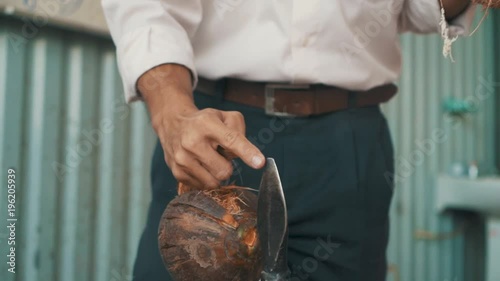 Vietnamese man gestures to to the tip of a spear used to split open coconuts while holding two coconuts