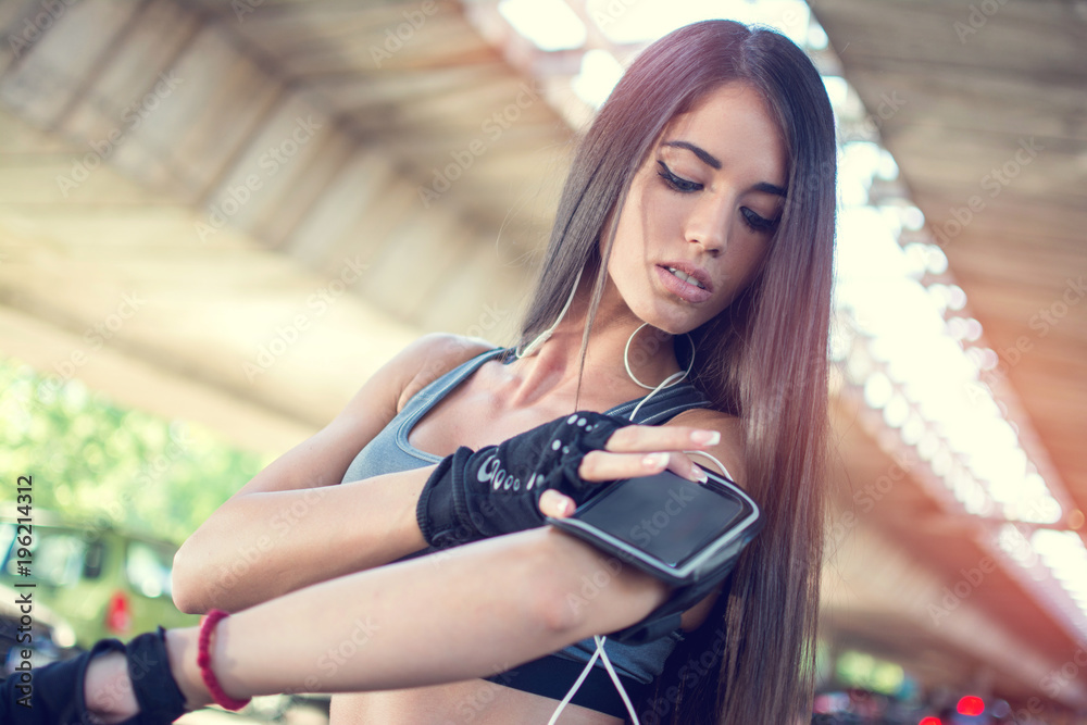 Portrait of young woman touching smartphone on armband outdoors.