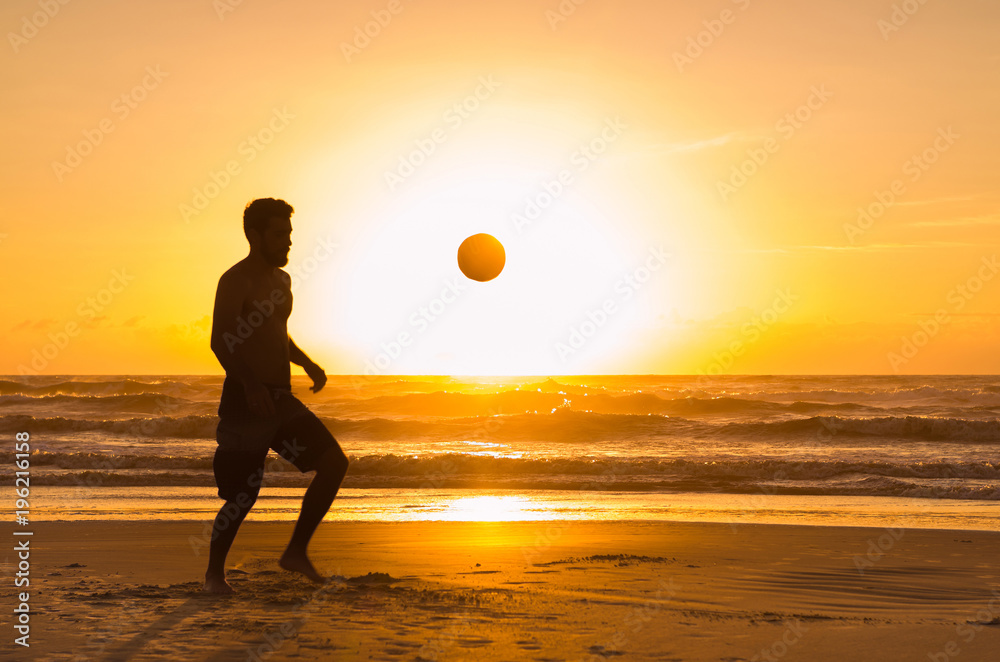 Great concept of soccer, man playing soccer on the beach in golden hour, sunset. Making keepie uppie.