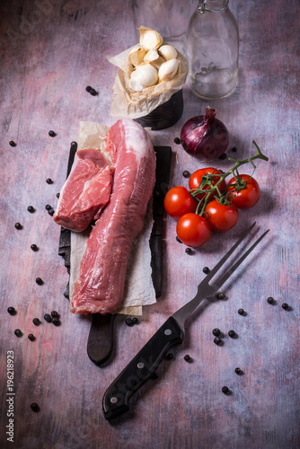 Whole pork tenderloin meat on vintage board with garlic and tomatoes