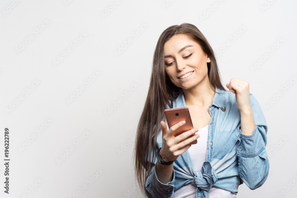 Portrait of young smiling woman with pink smartphone receiving some great news over white background. Lifestyle, people and technology concept. Portrait of young smiling woman with pink smartphone receiving some great news over white background. Lifestyle, people and technology concept.
