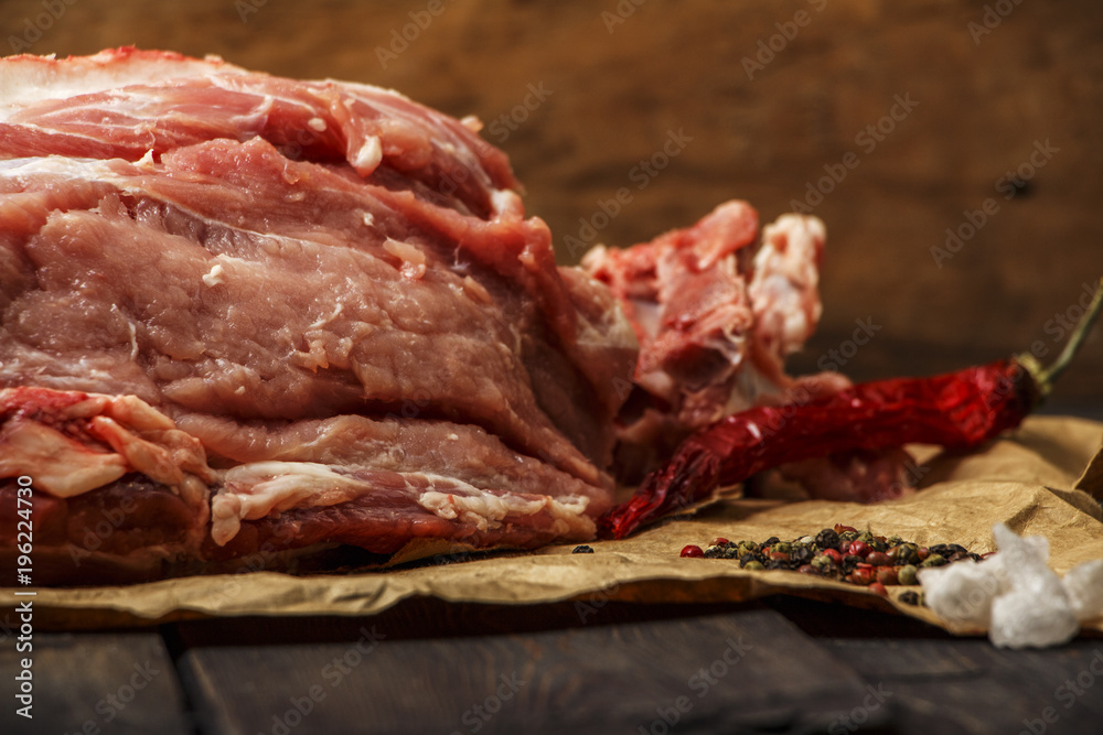 Fresh pork raw meat on a paper with spices on a dark wooden table. A piece of pork meat close-up. The meat is fresh. Selective focus.