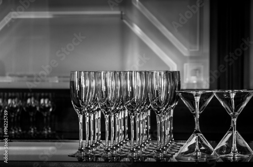 Clean wine and martini glasses sit shimmering on a bar in the right side. A geometric pattern is embedded in the mirror. Horizontal image in black and white.