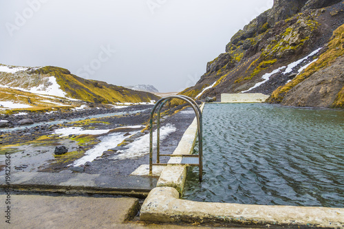 Natural swimming pool Seljavallalaug in iceland with man in water and snowy weather and mountains all around