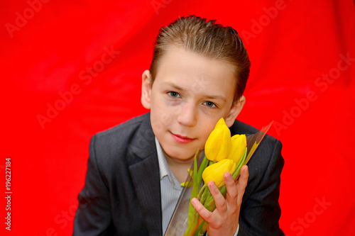 Boy in a suit with tulips on a red background. Photo portrait in the studio. photo