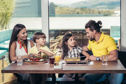 Father and mother with children enjoying meal in restaurant.