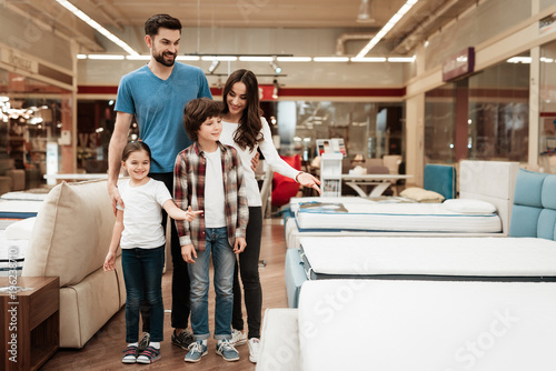 Happy family buys new orthopedic mattress in furniture store. Blissful family choosing mattresses in store.