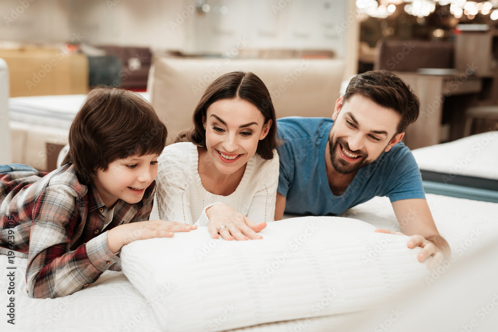 Young beautiful woman and bearded man with cute little boy lies on bed in mattress store. Young beautiful woman and bearded man with cute little boy lies on bed in mattress store.