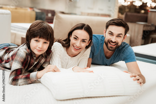 Young beautiful woman and bearded man with cute little boy lies on bed in mattress store.