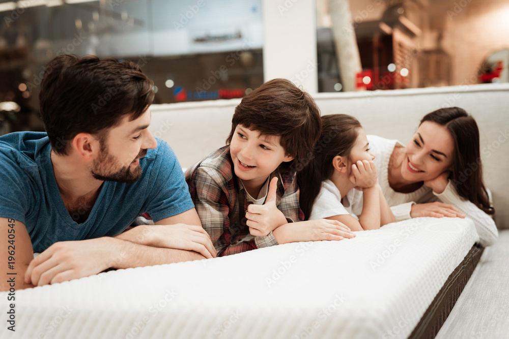 Young happy family checks on softness of orthopedic mattress, lying on bed in furniture store. Young happy family checks on softness of orthopedic mattress, lying on bed in furniture store.