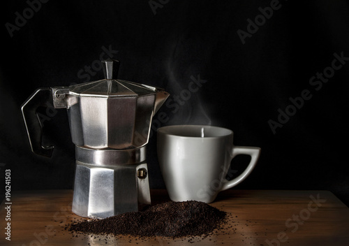 Italian coffee maker and a cup with hot drink over a wood table and a black background