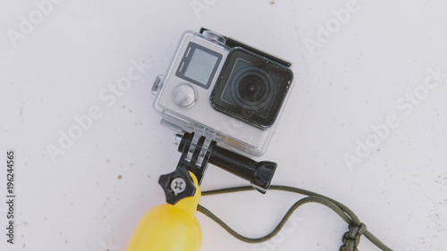 Modern action camera in the case lying on the  of the white surfboard. Camera for shooting in water with a float