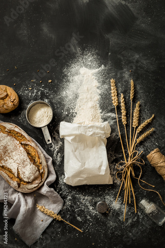 Bread, flour bag, wheat and measuring cup on black - kitchen