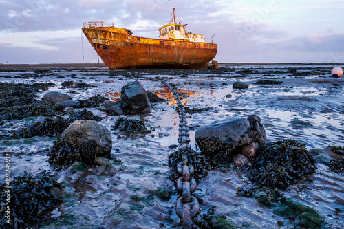 Rusty old fishing vessel marooned at low tide on a mud bank a long anchor chain