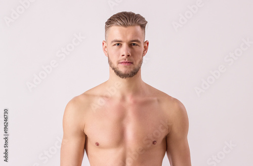 Studio shot of handsome naked man looking to camera while standing isolated on white background. Young bearded hipster standing against white background. Concept of men's masculinity and confidence
