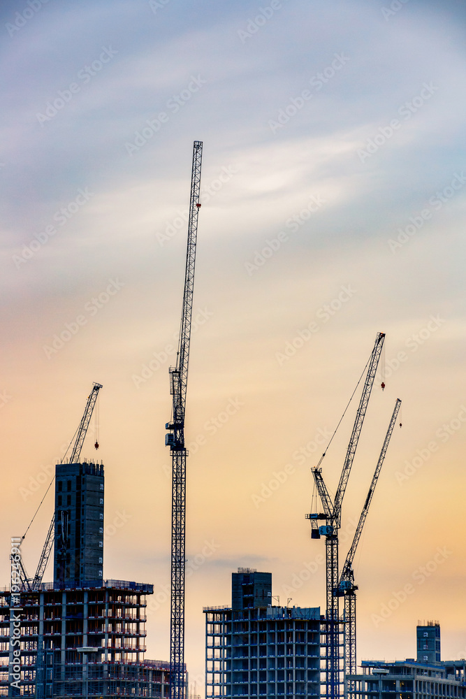 Silhouette of new skyscrapers under construction with tall cranes against colourful sky. Construction business and industry, urbanisation, urban sprawl real estate bubble concept.