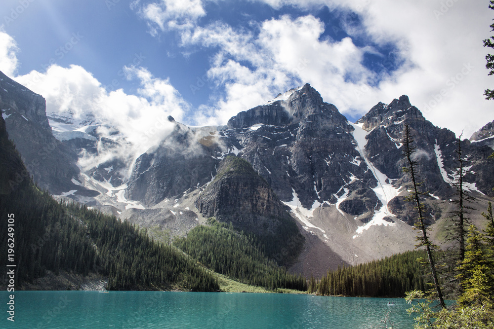 Fototapeta premium Standing on the shore with ice melt waters, mountain tops, trees and clouds