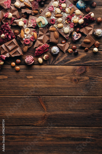 Pieces of chocolate with nuts and berries on rustic wooden background with copy space