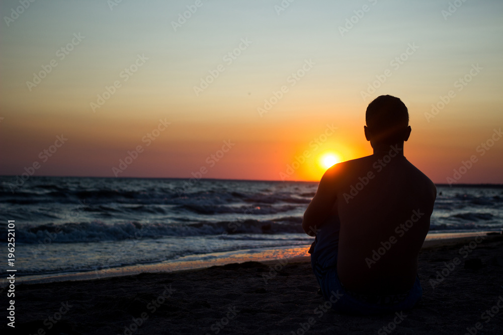 silhouette of a man who sits on the sand near the sea, in the rays of the setting sun near the sea. place under the text, relax on the sea