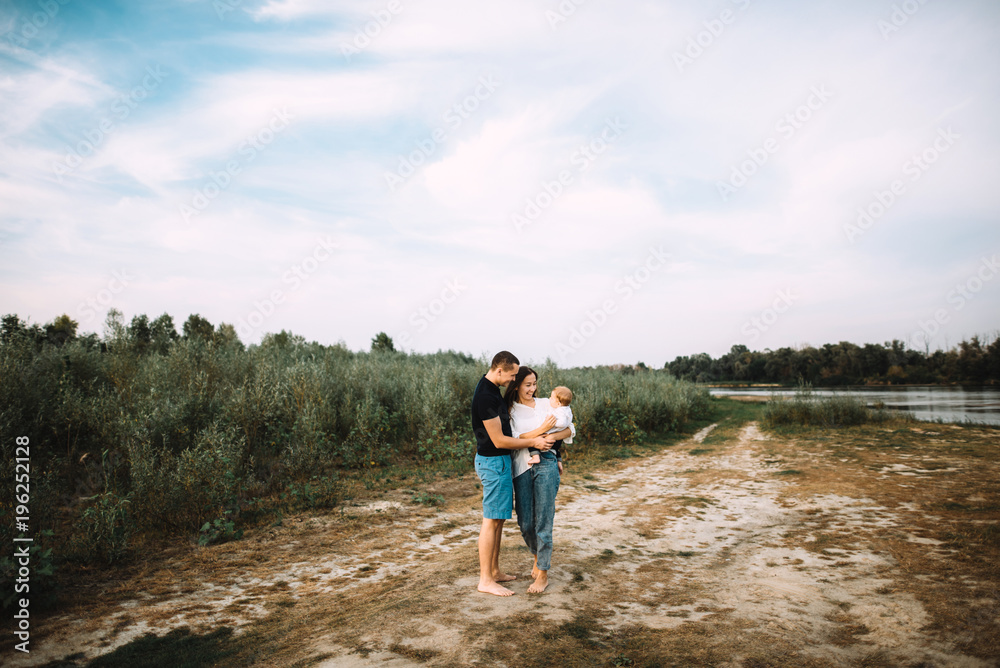 Happy young parents are walking in the countryside near the river with their little baby