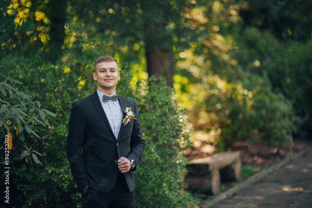 Handsome brunette groom stands on green lawn Handsome brunette groom stands on green lawn