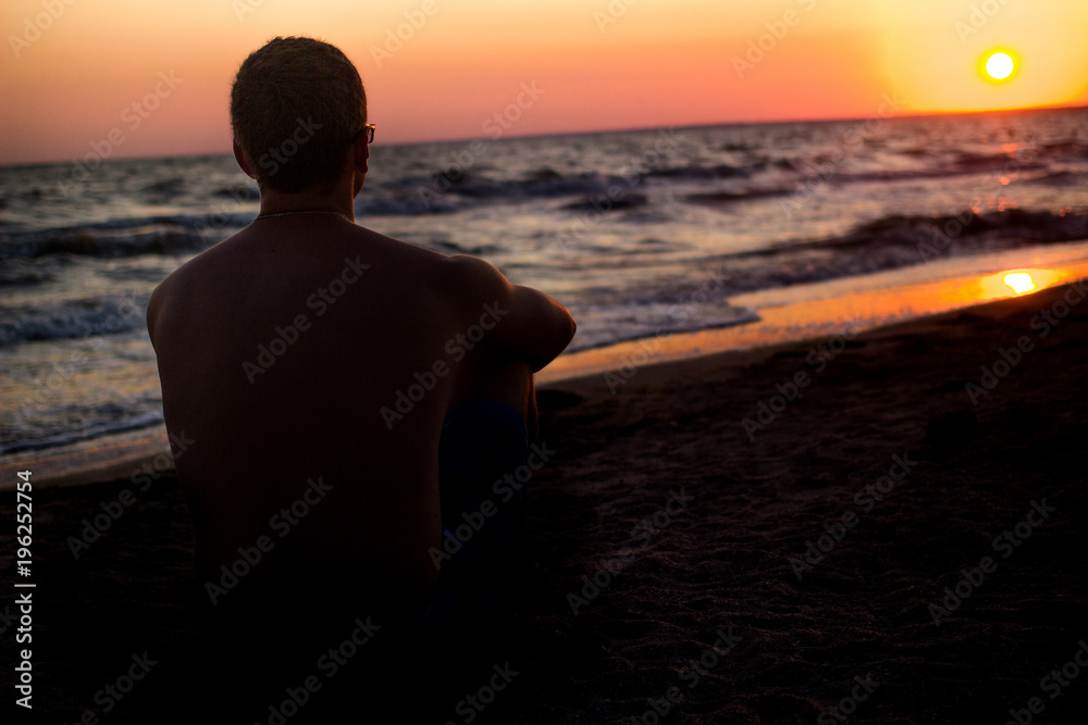 silhouette of a man who sits on the sand near the sea, in the rays of the setting sun near the sea. place under the text, relax on the sea