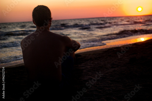 silhouette of a man who sits on the sand near the sea, in the rays of the setting sun near the sea. place under the text, relax on the sea