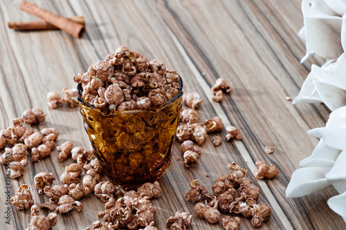 chocolate flavored popcorn in the yellow glass and on the brown wood table with cinnamon background