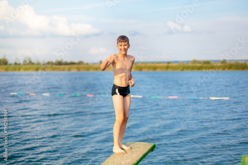 sporty cute young boy jumps very high from pier and having fun on his vacation by the sea