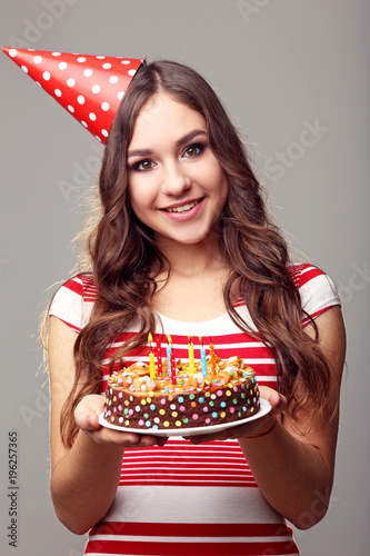 Young woman holding cake with candles on grey background