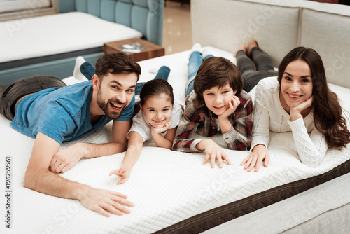 Happy family is relaxing on mattress in orthopedic furniture store. Big family check softness of mattress