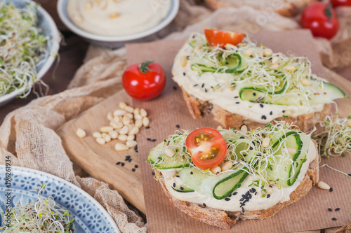 Healthy vegetarian bruschettas with bread, micro greens, hummus, cherry tomatoes, cucumbers and pine nuts