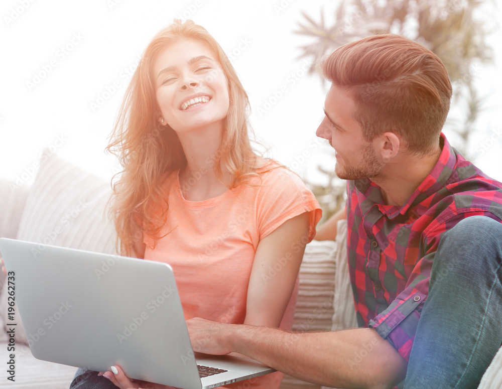 young couple is using a laptop and smiling while sitting on sofa at home young couple is using a laptop and smiling while sitting on sofa at home